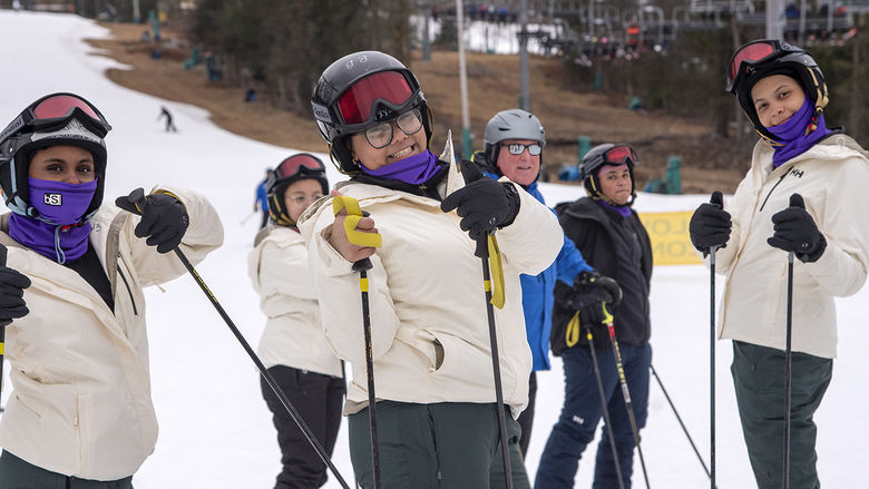 Students in white winter coats holding ski poles while standing on a snow slope.