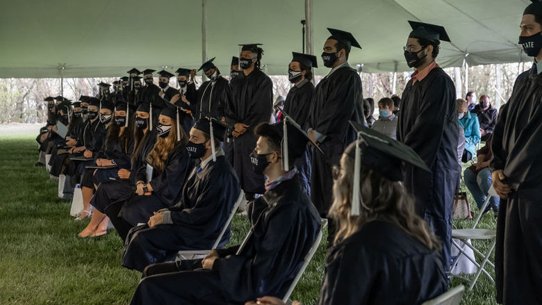 Two rows of graduates in caps and gowns underneath a tent.