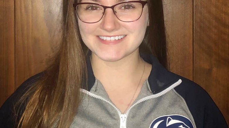 Female student in front of brown wall wearing Penn State sweatshirt