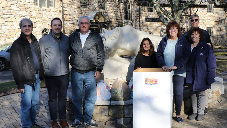 Group of men and women lined up outside in front of Nittany Lion statue and cardboard box full of food donations.