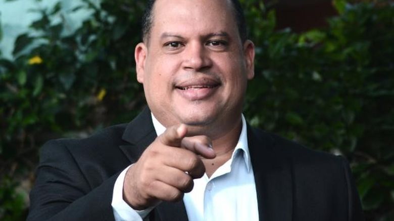 Hanglet Tejada in suit and jacket pointing with index finger.