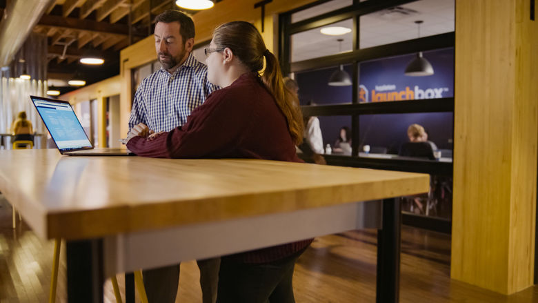 Two people standing beside a long wooden desk.