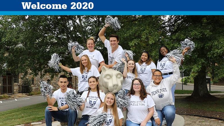 A group of male and female students shaking pom poms and sitting by a lion statue. 