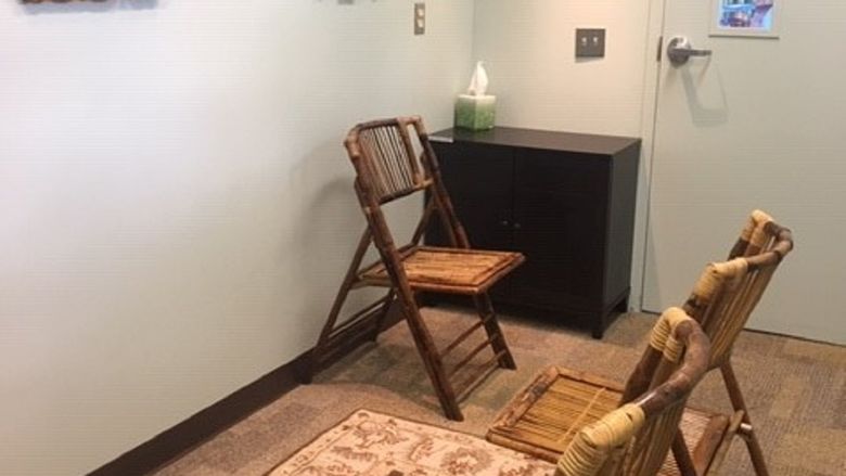 Small room with chairs, a shelf and lamps with brown carpeting 