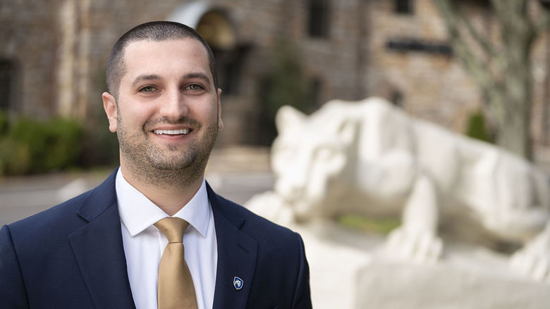 Man in a suit and tie smiling in front of Nittany Lion statue.