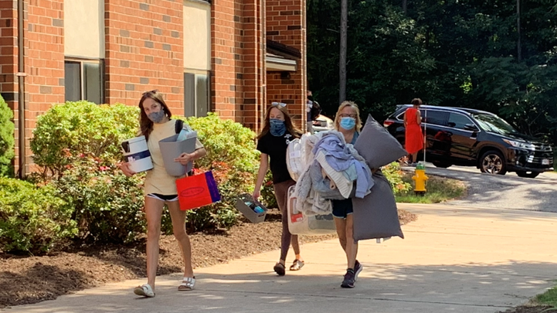 Students and a parent carrying boxes and other belongings on a sidewalk into North Hall