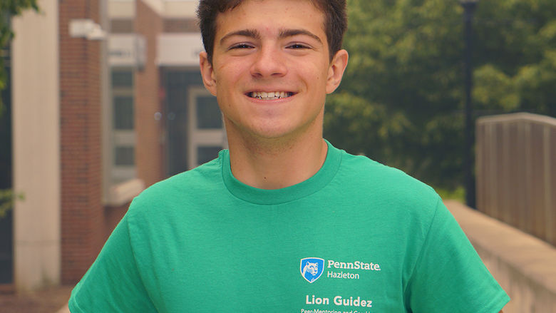 Male student in green Penn State shirt standing on a sidewalk.