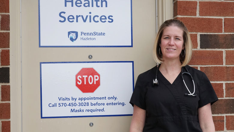 Woman in scrubs standing in front of office door with signs denoting campus health services.