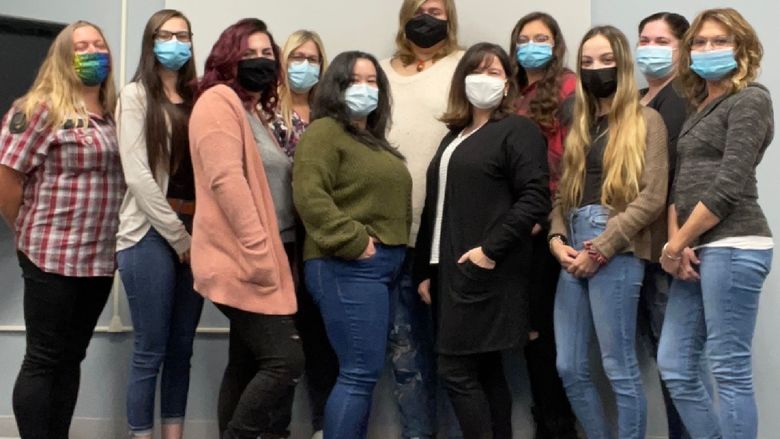 Group of women wearing masks and standing in a row inside a classroom.