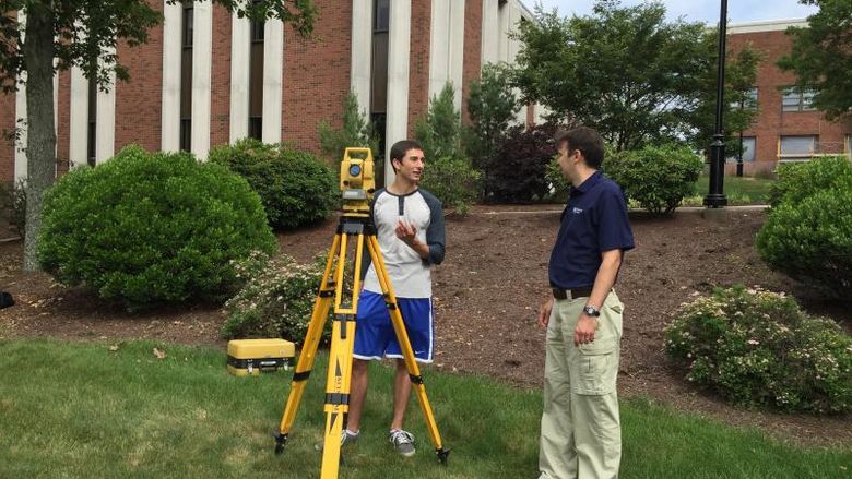 A student looks through surveying equipment as an instructor looks on.