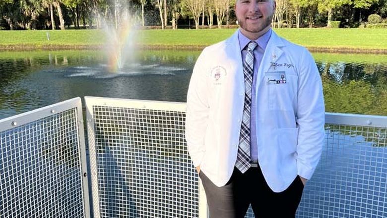 Man in white doctor's jacket standing on balcony in front of a pond with a water fountain gushing from inside it.