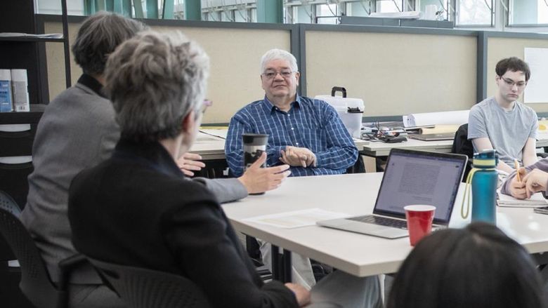 A man sitting at a table listening to someone on his right speak as others at the table look on.