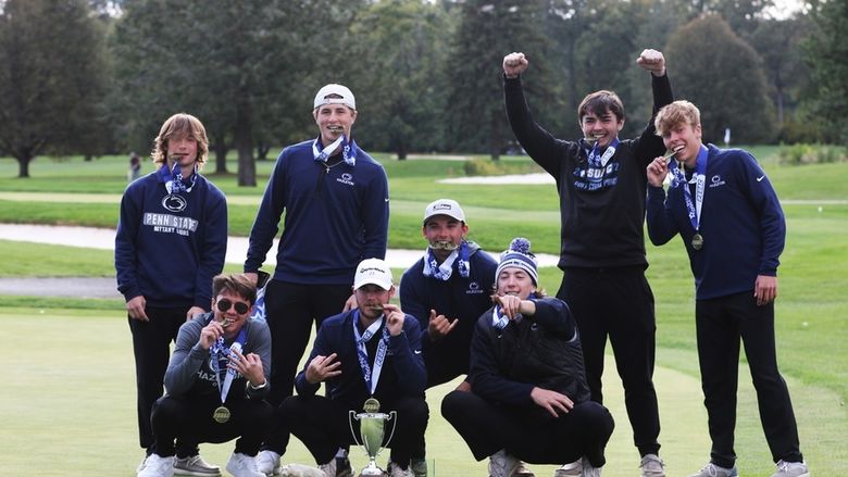 Group of eight students on a golf course holding golden medals and celebrating.