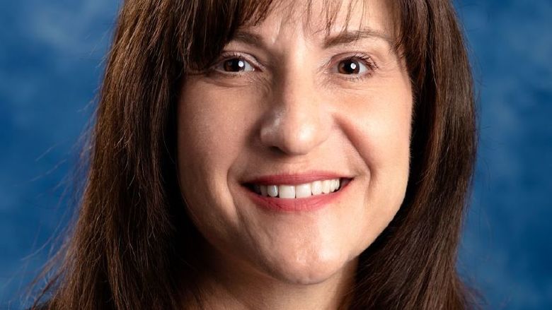 Woman with brown hair wearing a white shirt with black sweater over it.