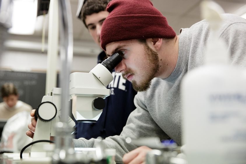 A student looking through a microscope in a classroom.