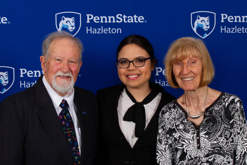 Man and woman standing with female student in between them.