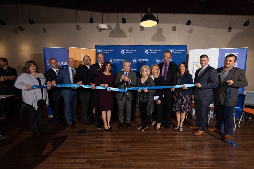 A group of eleven people lined up and holding a ribbon with one person cutting it. 