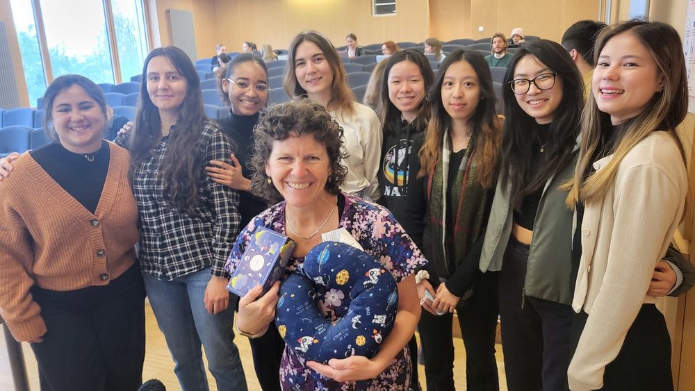 A group of females with their professor, another woman, crouching in front holding gifts.