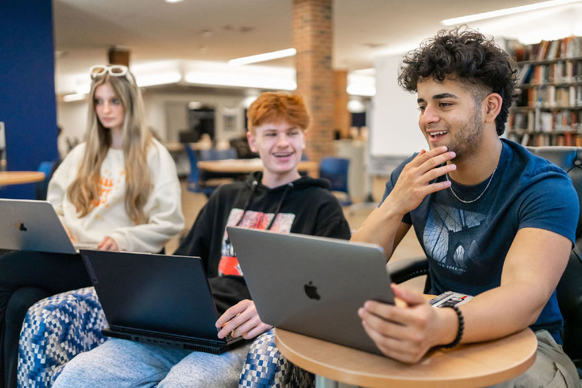 Three students seated and laughing in conversation with each other in a library.