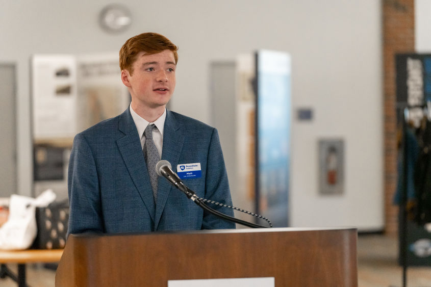 Student in a suit speaking from a wooden podium.