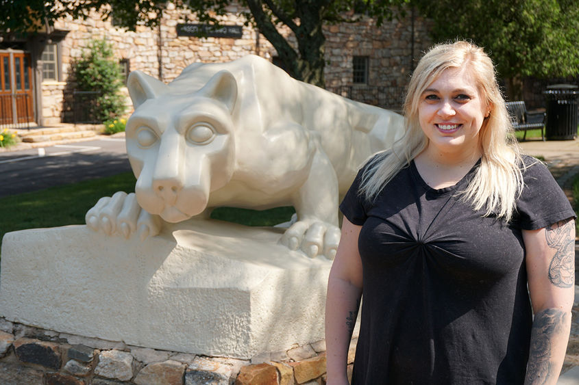 Woman in black dress standing next to statue of Nittany Lion on Penn State Hazleton campus.