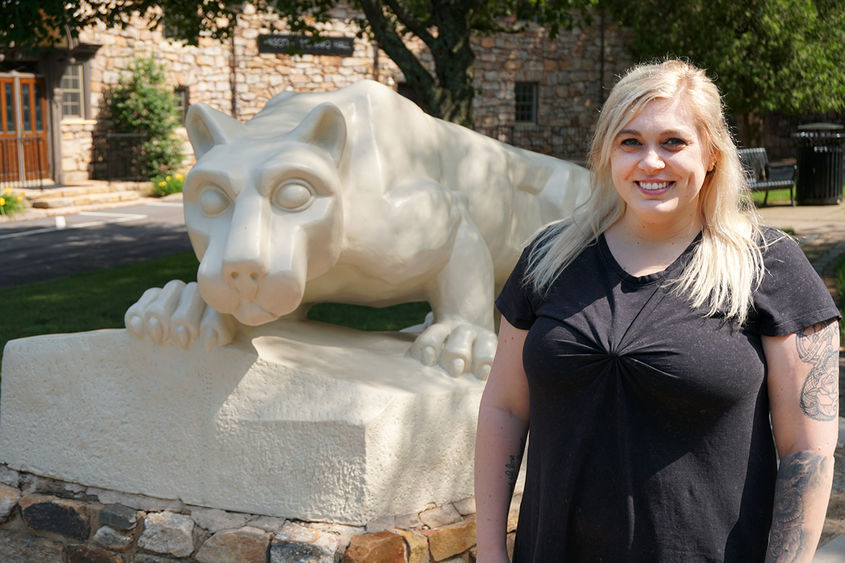 Alyssa Schuetrum Woman in black dress standing next to statue of Nittany Lion on Penn State Hazleton campus.