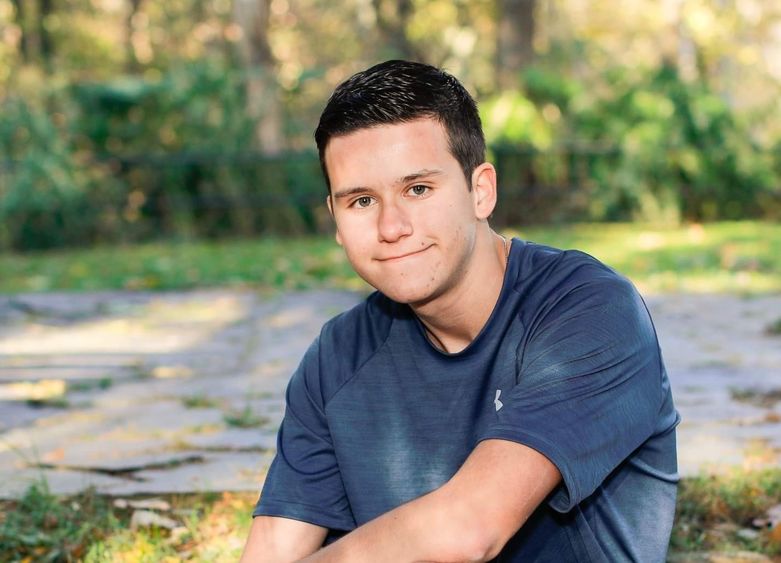 Male student seated outdoors on a rock wearing shorts and a T-shirt.