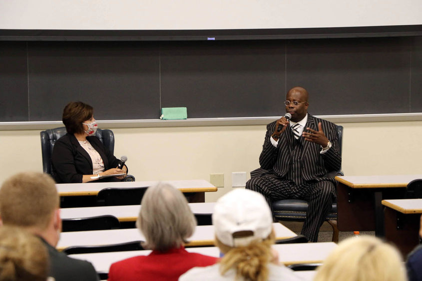 Man with microphone answering a question in a classroom with female moderator seated next to him.