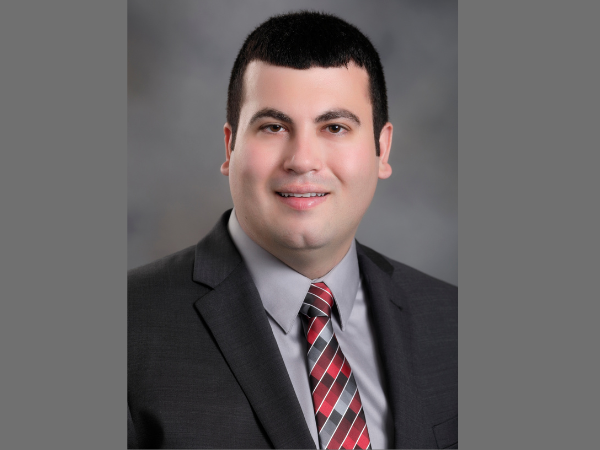 Man with dark hair in a black suit jacket, grey dress shirt and striped tie.