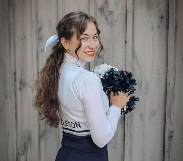 Cheerleader smiling and holding pom-pom.