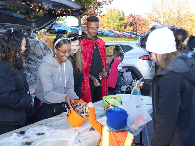 Students in Halloween costumes handing out candy to child in a costume.