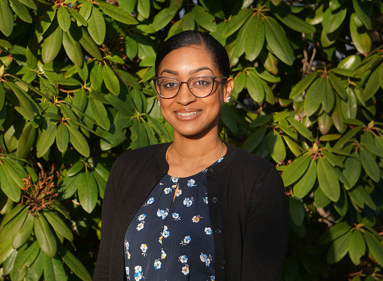 Woman smiling in front of green bushes.