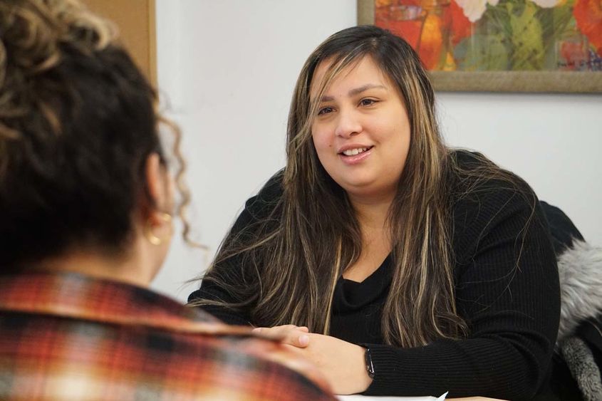 Woman seated at desk speaking with student seated across from her.