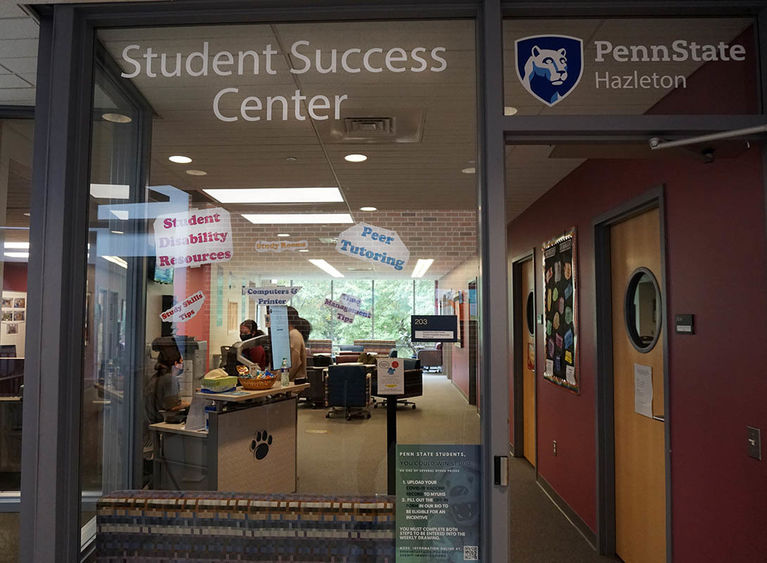 Glass window looking into room with students gathered around a desk.