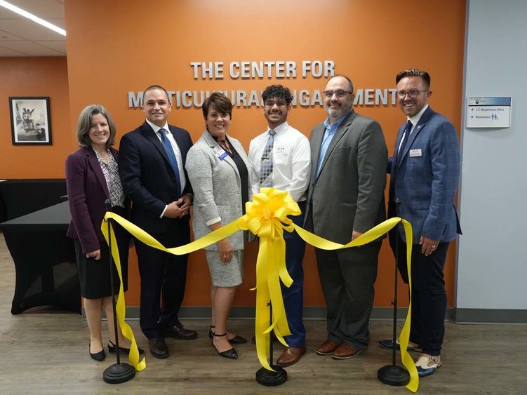 Group of six people standing in front of a yellow ceremonial ribbon.