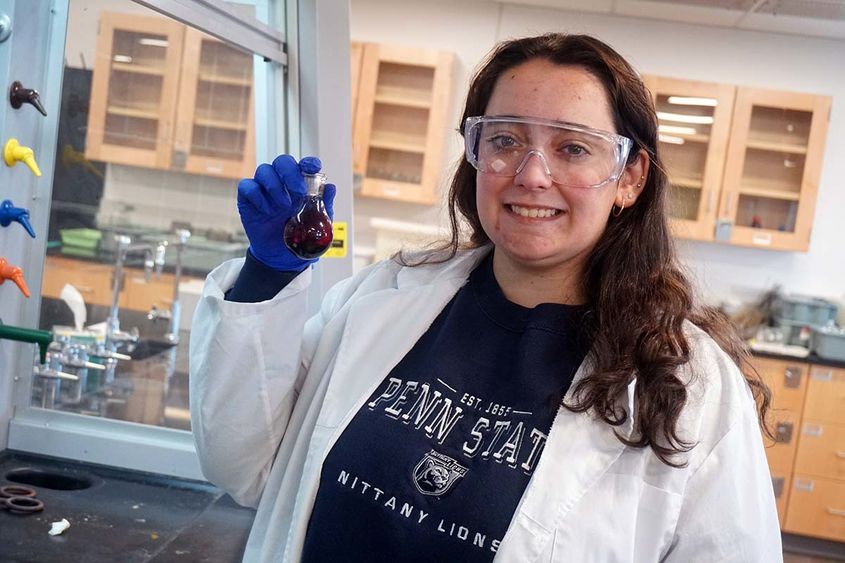 Woman in lab coat holding beaker of purple liquid in a science laboratory.