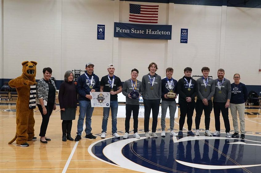 Group of 12 people lined up in a row on a basketball court with seven of them wearing championship medals.