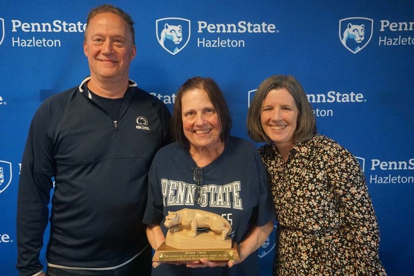 Woman holding miniature Nittany Lion statue standing next to another man and woman.