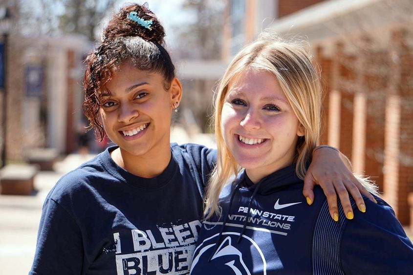 Two female students smiling on a college campus.