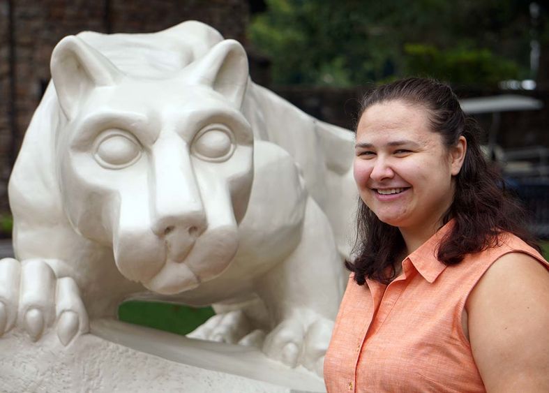 Woman with brown hair and salmon-colored blouse smiling next to stone statue of a lion.