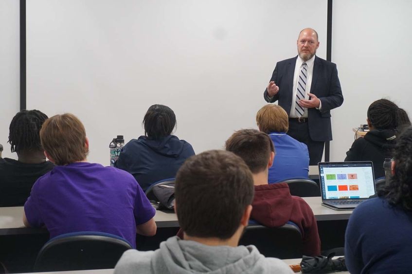 Man in a suit speaking to students in a classroom