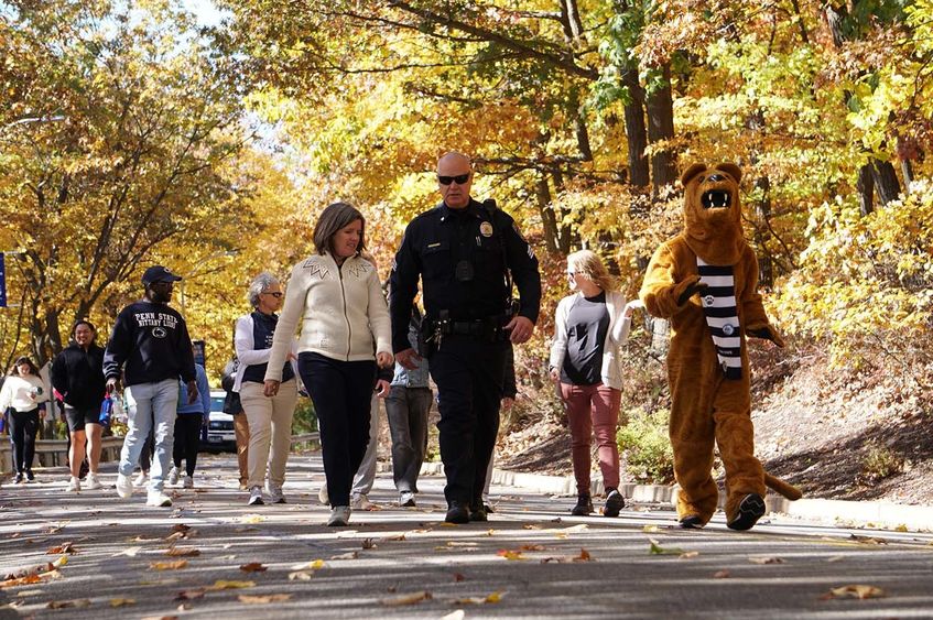 Group of people walking downhill on a road surrounded by fall foliage.