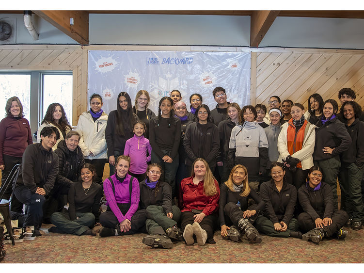 Group of about 30 people inside a clubhouse room at a ski resort dressed in ski gear.