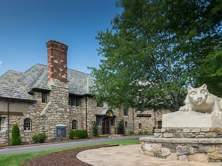 Brick mansion with statue of Nittany Lion in foreground.