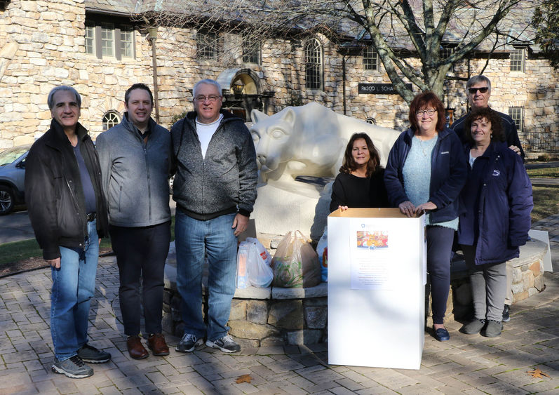 Group of men and women lined up outside in front of Nittany Lion statue and cardboard box full of food donations.