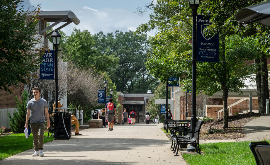 Students walking on a sidewalk at a college campus on a sunny day.