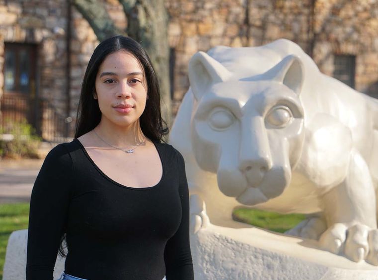 Woman with dark hair standing next to cream-colored Nittany Lion statue.