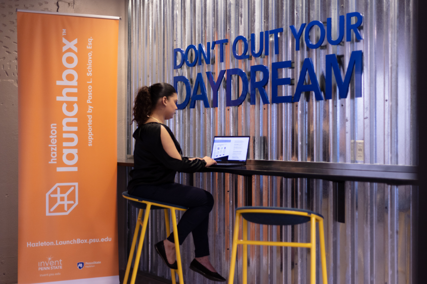 An individual is working at the Hazleton LaunchBox under a "Don't Quit Your Daydream" sign.