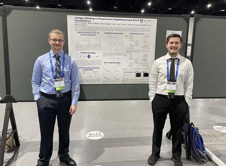 Two students standing in front of a white poster board.