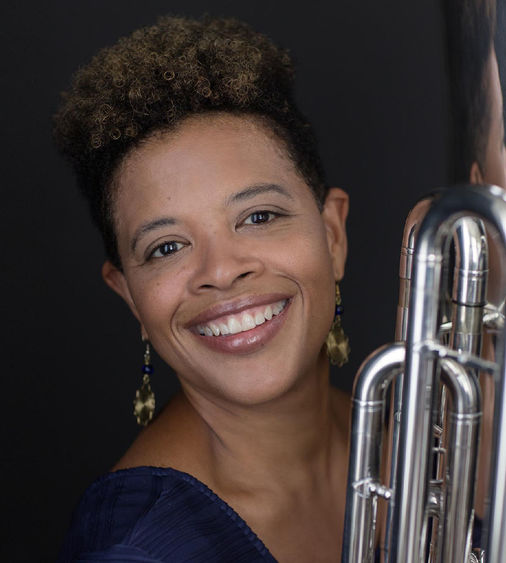 Woman with brown hair smiling and holding a tuba.